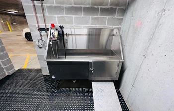 A stainless steel box with a red handle is placed on a black rubber mat.